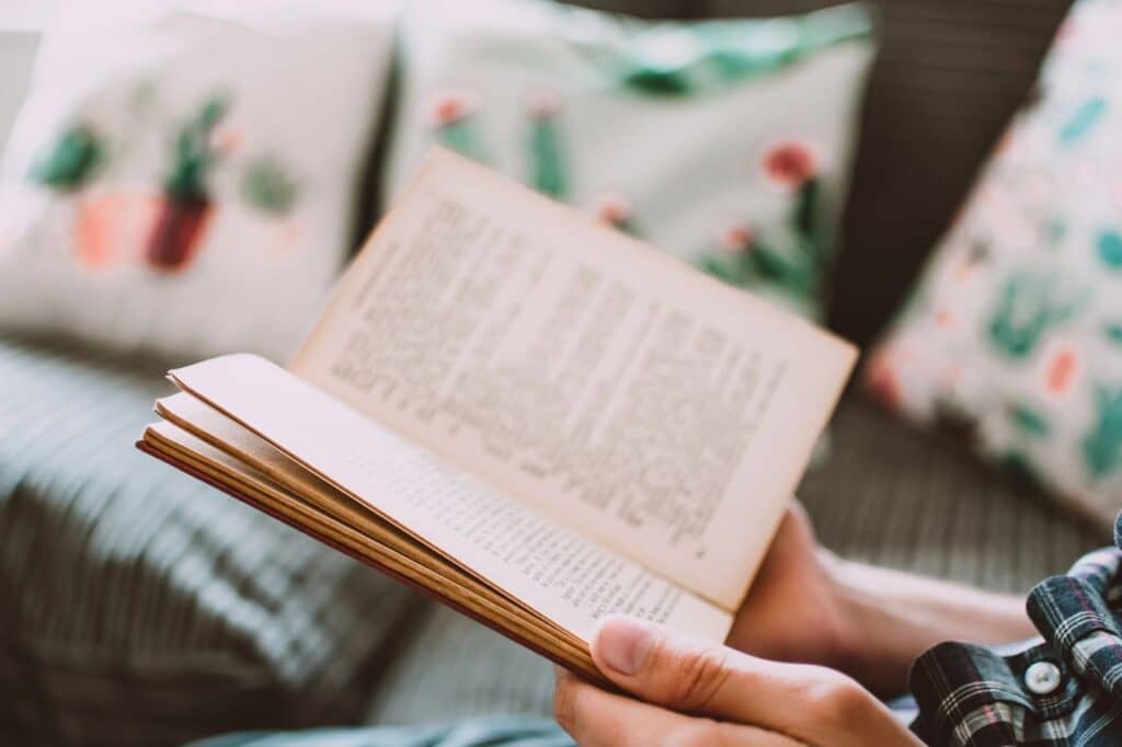 Une personne tient un livre ouvert et lit, assise dans un intérieur.